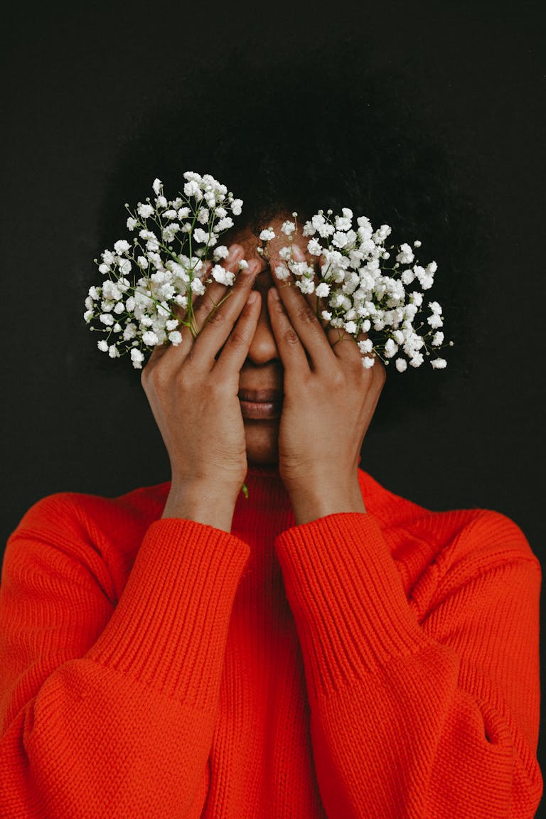Artistic portrait of a woman covering her eyes with white flowers, against a dark background.
