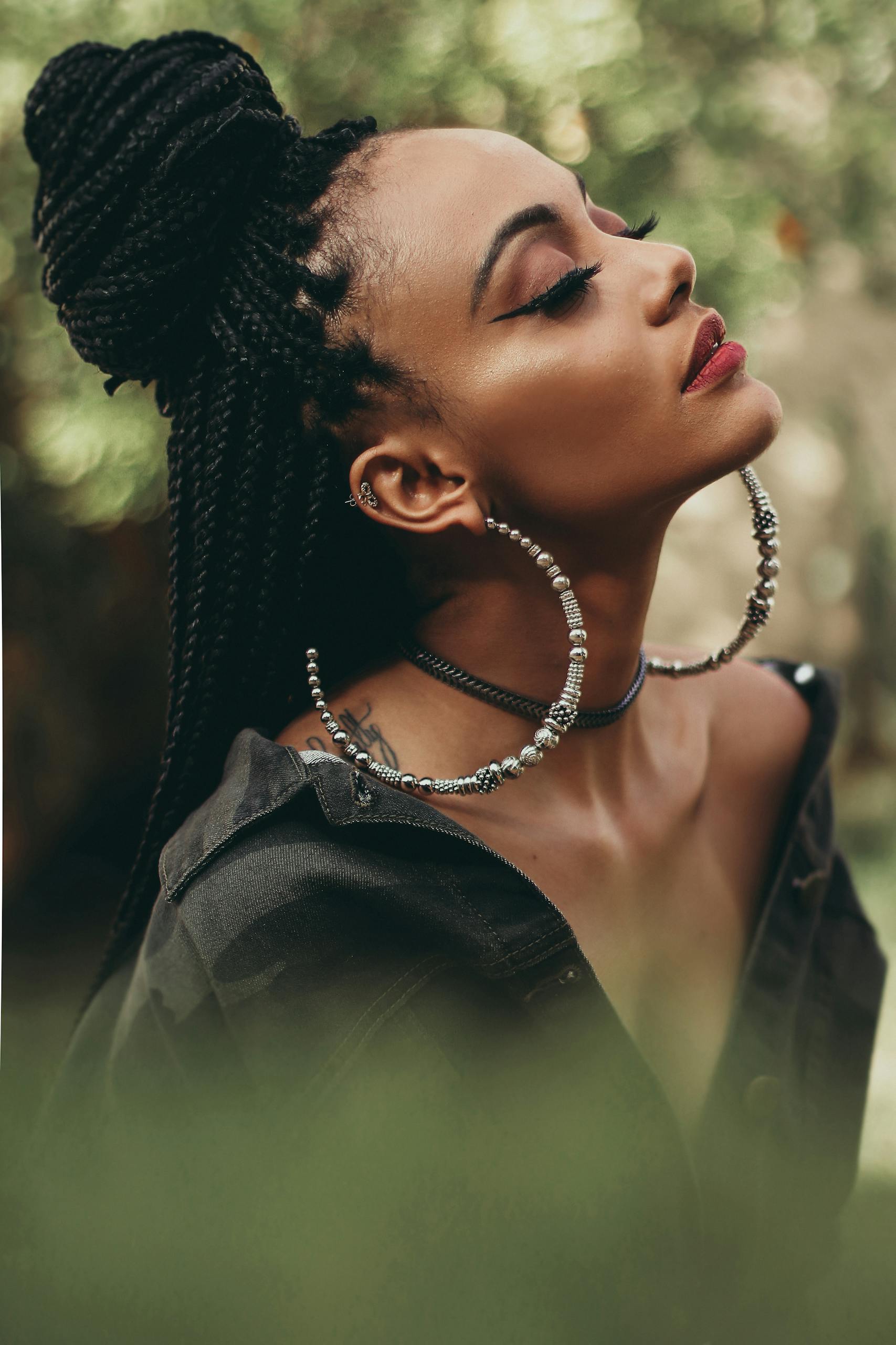 Captivating portrait of a woman with braided hair and stylish jewelry posing outdoors.