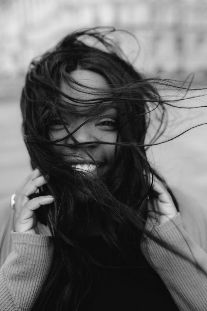 A black and white portrait capturing the joyful smile of a woman with hair blowing in the wind.