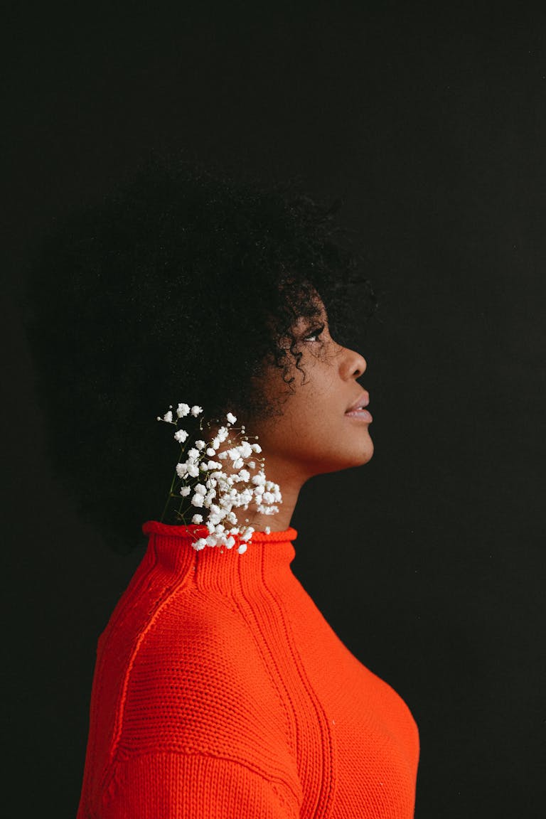 Side profile of a woman with afro hair and white flowers against a black background.