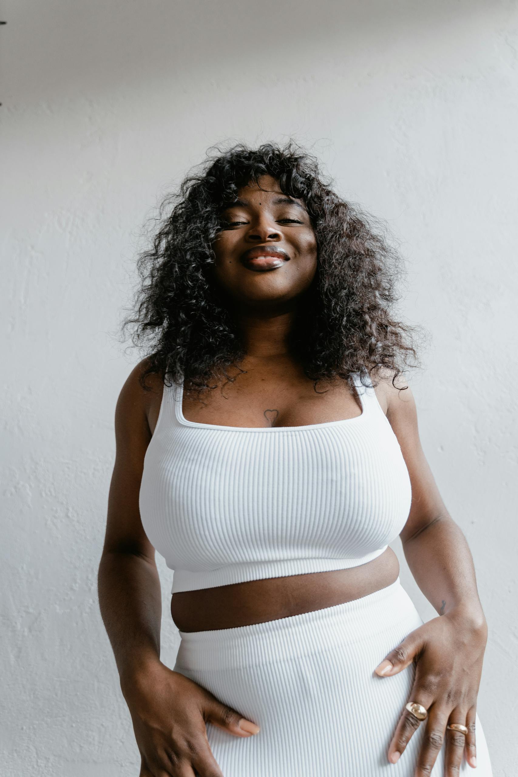 Stylish plus-size African American woman smiling confidently in a white tank top.